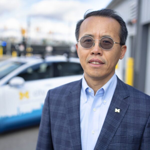 Henry Liu stands in front of an autonomous vehicle at the Mcity Test Facility