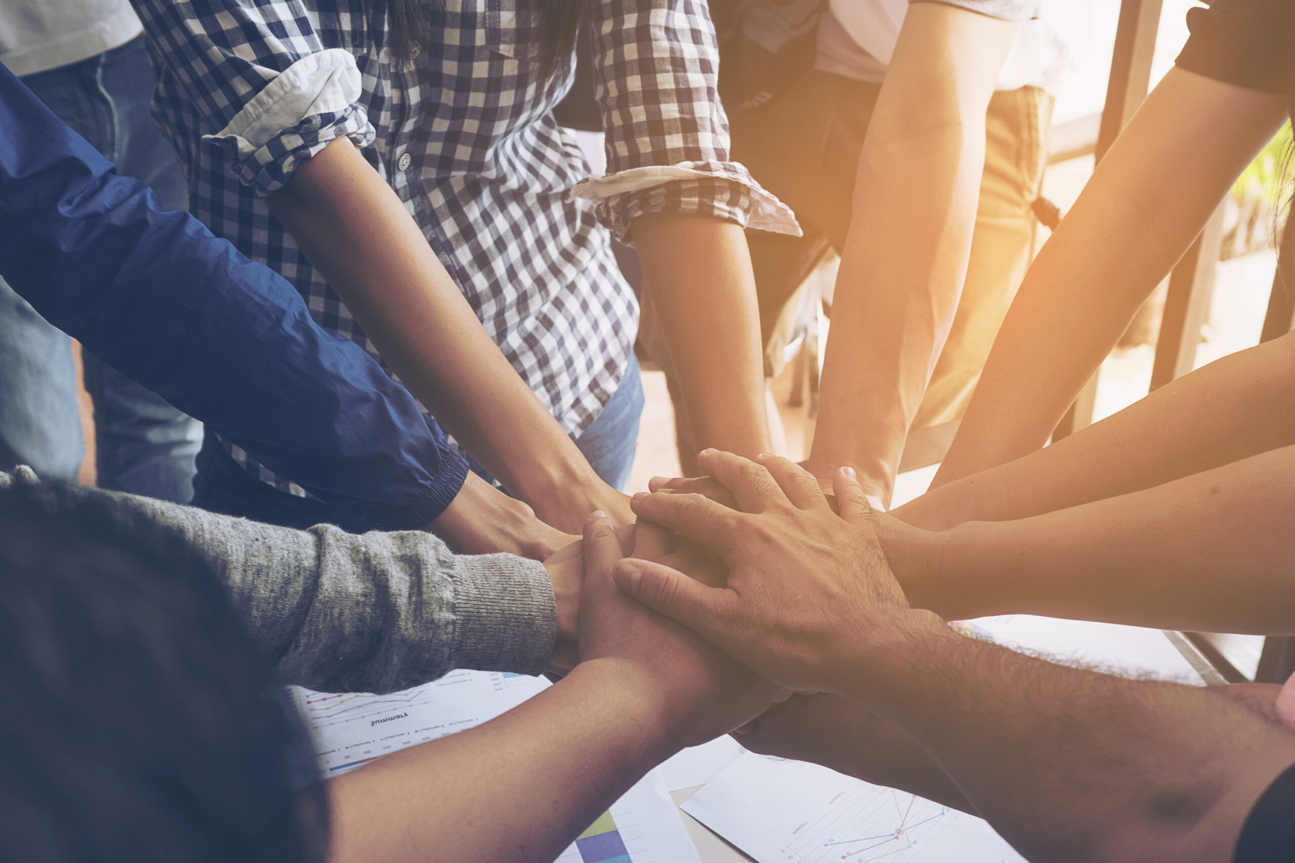 People joining hands in center of huddle, representing teamwork.