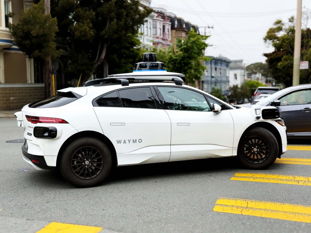A Waymo robotaxi drives through an urban environment
