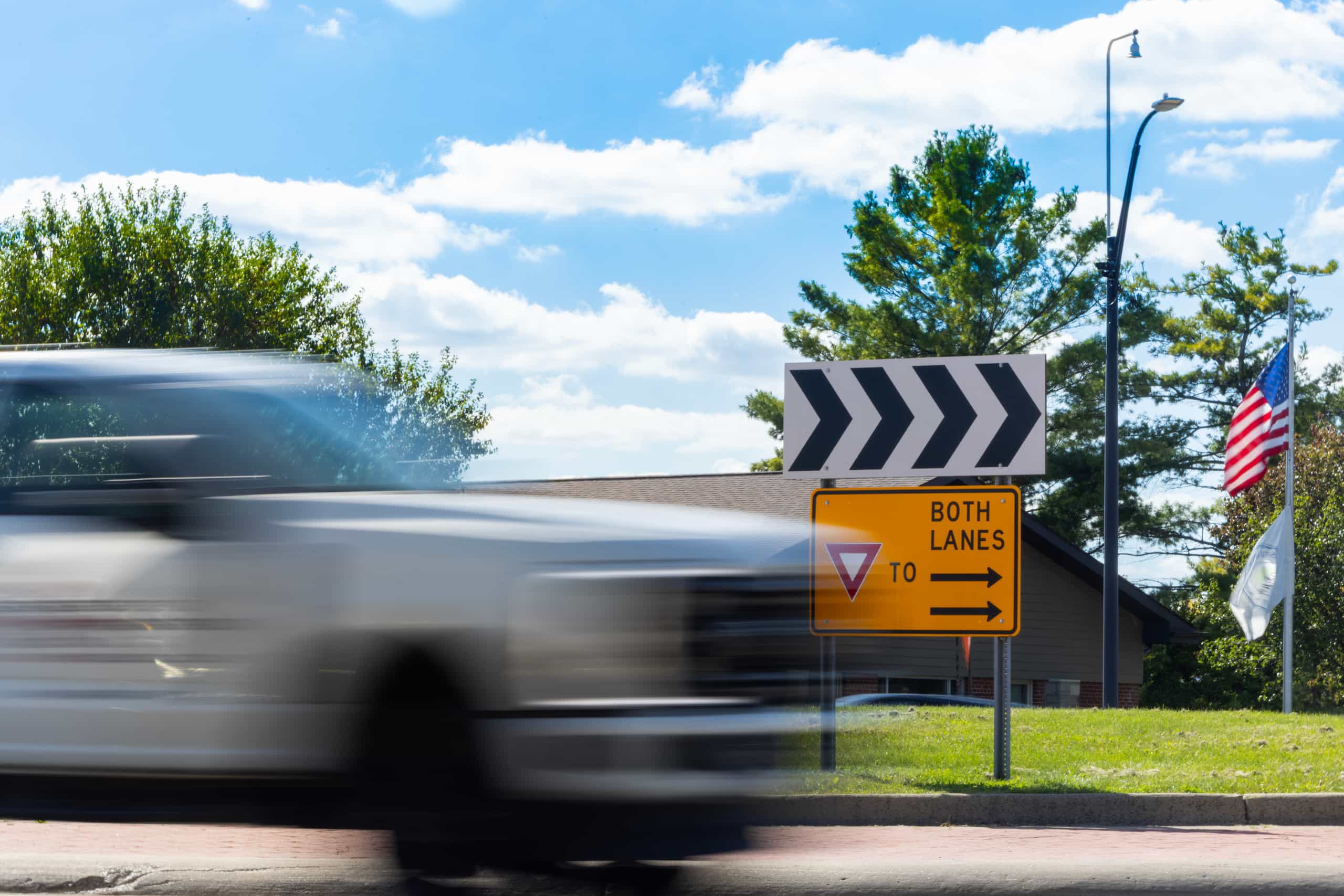 A motion blurred pickup truck moves past a yellow road sign that says yield to both lanes.